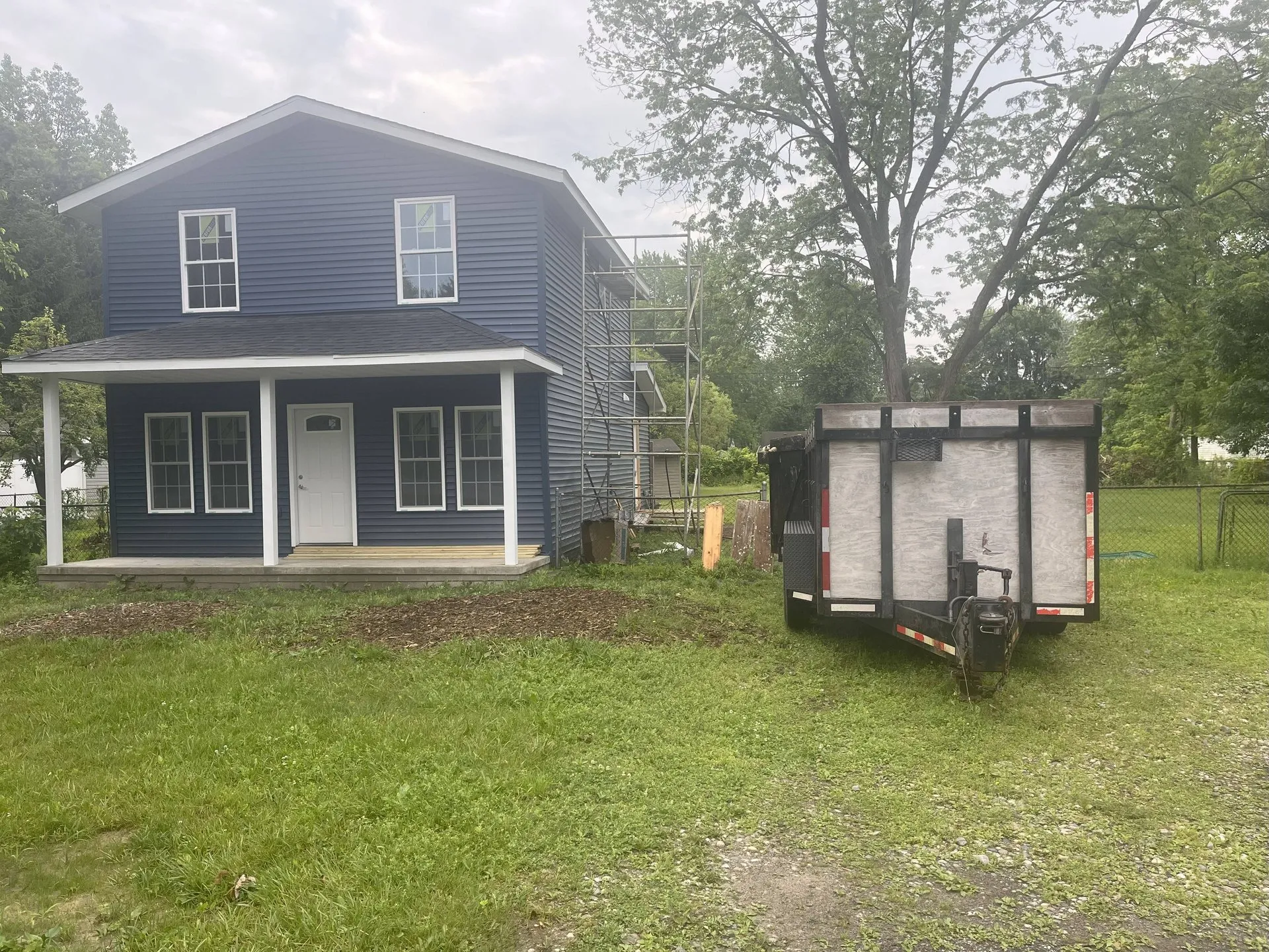 Dumpster trailer parked on the lawn beside a two story home during a renovation
