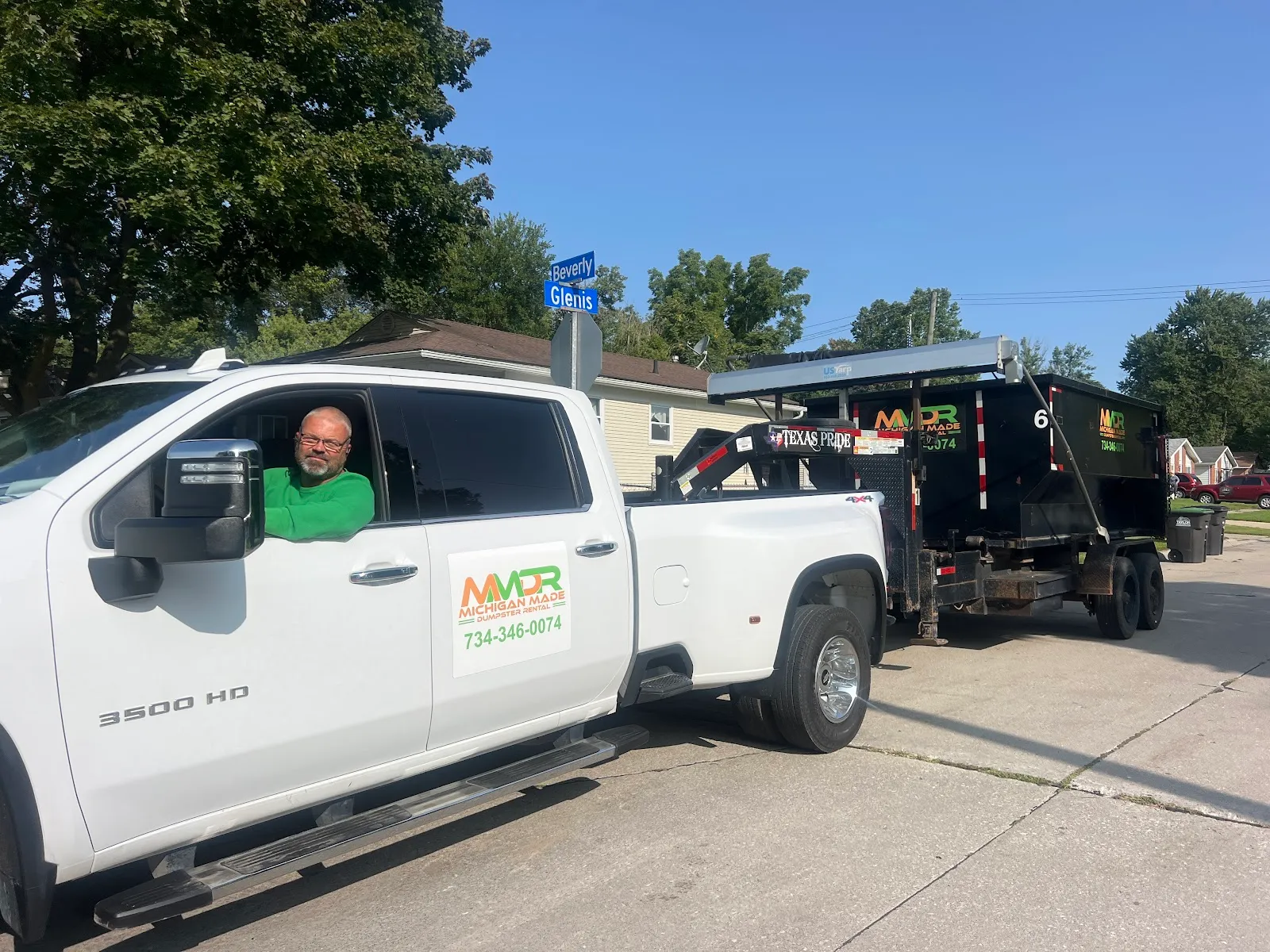 Owner of Michigan Made Dumpster Rentals in the company Silverado 3500 HD towing a dumpster trailer through a Wayne County neighborhood